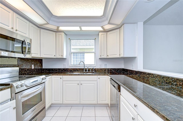 kitchen featuring appliances with stainless steel finishes, a raised ceiling, white cabinets, and a sink