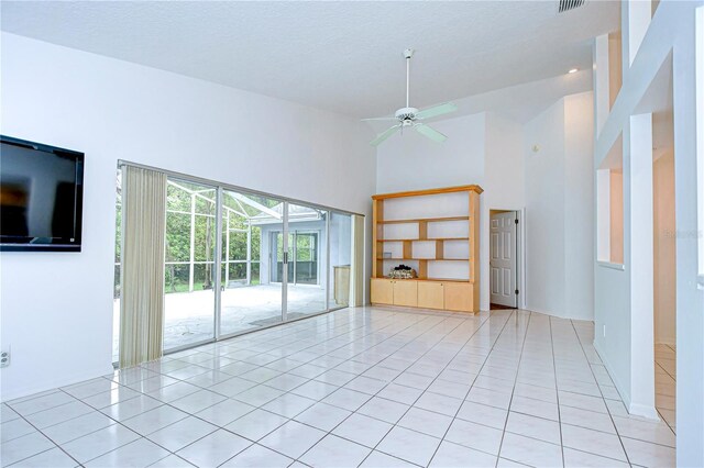 empty room featuring a towering ceiling, light tile patterned floors, ceiling fan, and a sunroom