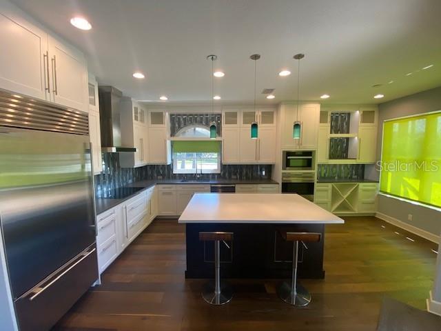 kitchen with tasteful backsplash, appliances with stainless steel finishes, white cabinetry, wall chimney range hood, and a kitchen breakfast bar