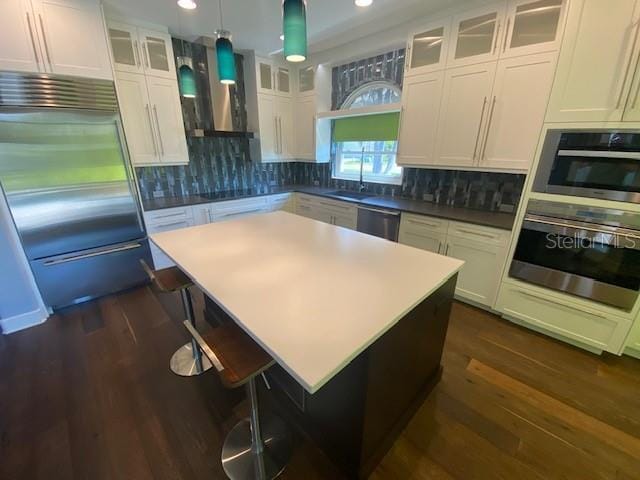 kitchen with dishwashing machine, dark wood-type flooring, stainless steel built in fridge, white cabinetry, and backsplash