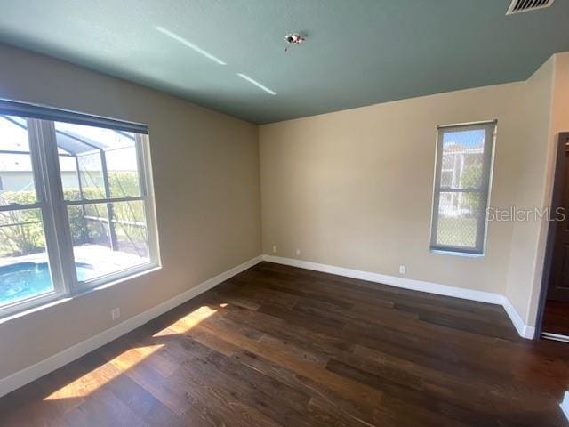 empty room with dark wood-style floors, visible vents, and baseboards