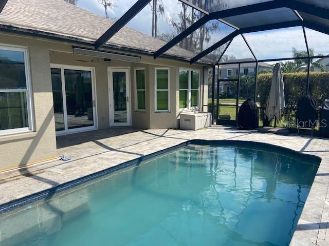 outdoor pool featuring glass enclosure and a patio