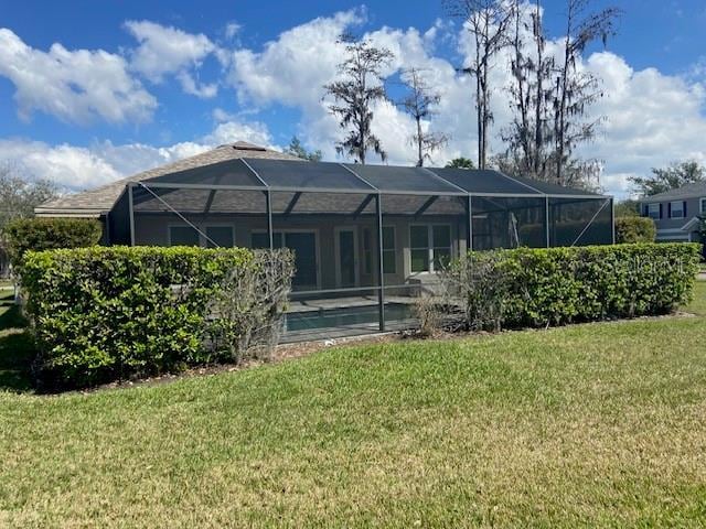 rear view of house featuring an outdoor pool, glass enclosure, and a lawn