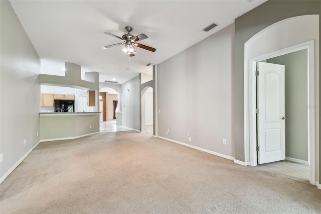 unfurnished living room featuring arched walkways, light colored carpet, a ceiling fan, baseboards, and visible vents