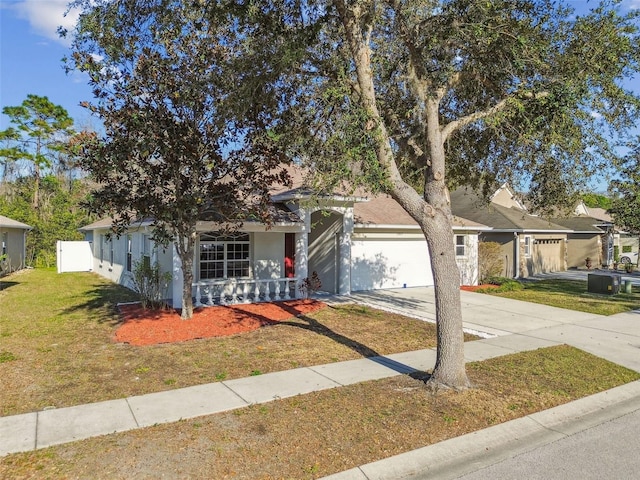 view of property hidden behind natural elements featuring a front lawn, concrete driveway, an attached garage, and stucco siding