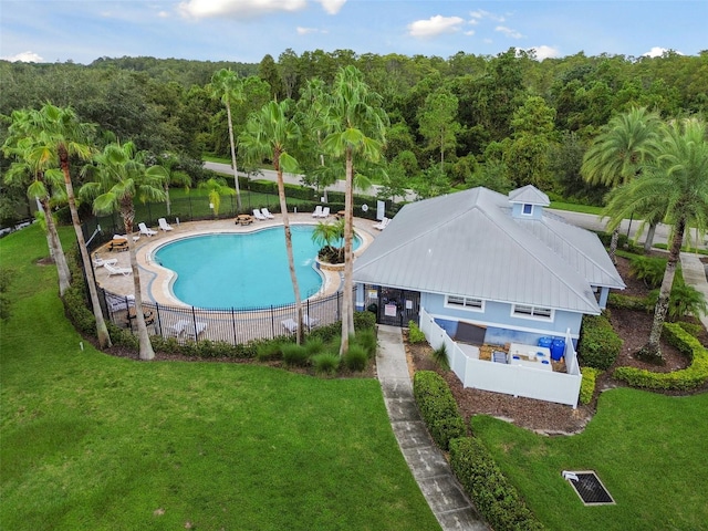 community pool featuring a yard, fence, a view of trees, and a patio