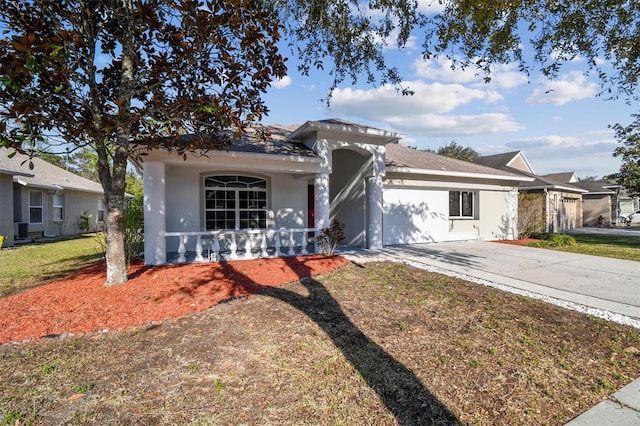 ranch-style home with covered porch, a front yard, concrete driveway, and stucco siding