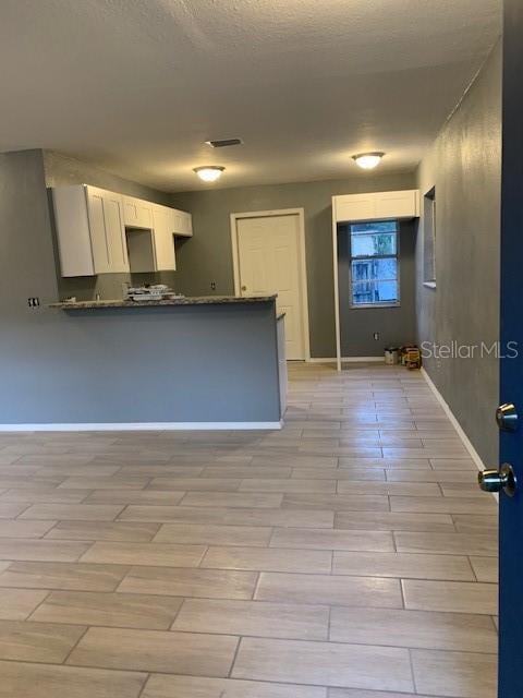 kitchen with dark countertops, visible vents, white cabinetry, a peninsula, and baseboards