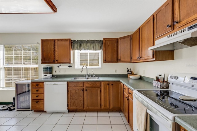 kitchen featuring brown cabinetry, light tile patterned flooring, a sink, white appliances, and under cabinet range hood