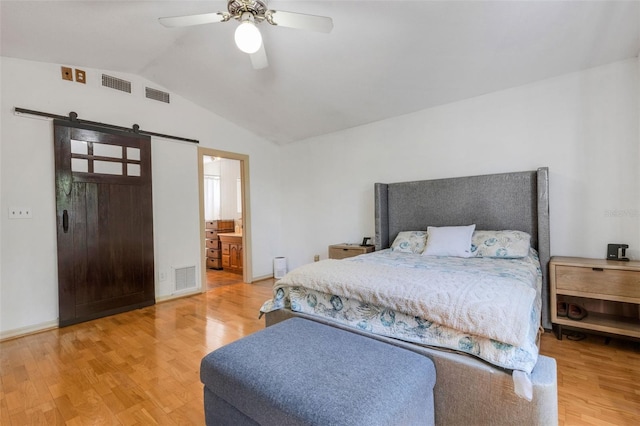 bedroom featuring lofted ceiling, a barn door, visible vents, and wood finished floors