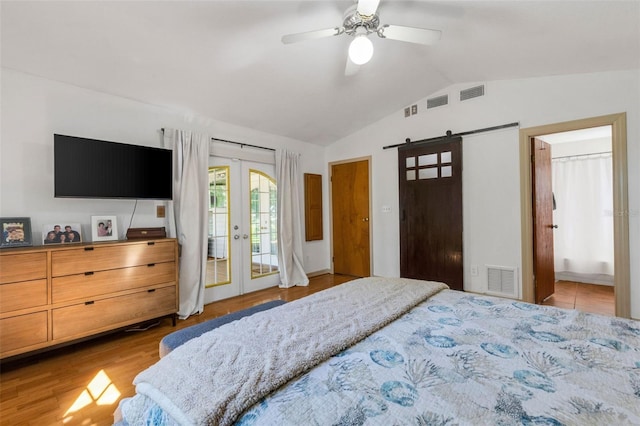 bedroom with a barn door, wood finished floors, visible vents, vaulted ceiling, and french doors