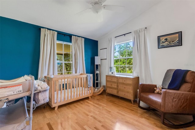 bedroom with lofted ceiling, light wood finished floors, a crib, and a ceiling fan