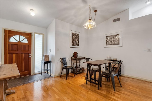 dining room with baseboards, visible vents, vaulted ceiling, light wood-type flooring, and a chandelier