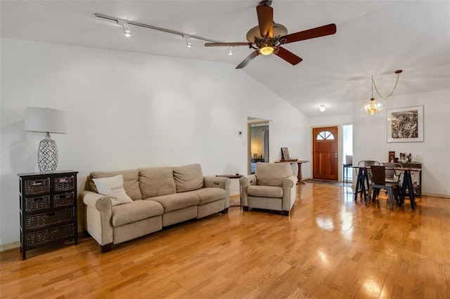 living area with light wood finished floors, ceiling fan with notable chandelier, vaulted ceiling, and rail lighting