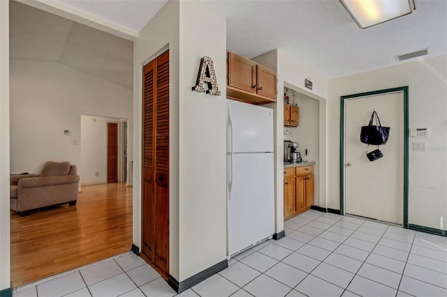 kitchen with light tile patterned floors, visible vents, lofted ceiling, freestanding refrigerator, and light countertops