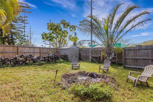 view of yard with an outdoor fire pit, a fenced backyard, a storage unit, and an outbuilding