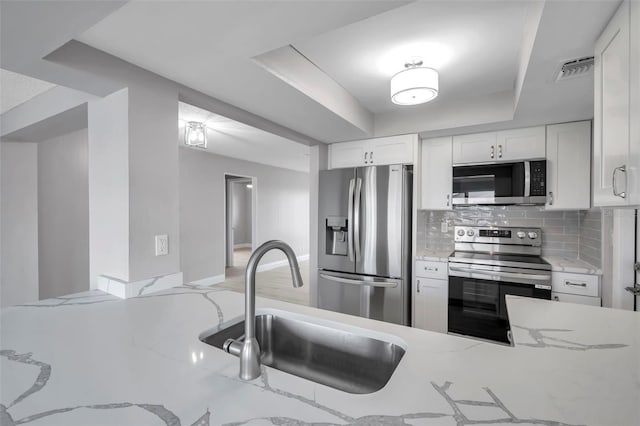 kitchen with a sink, white cabinetry, appliances with stainless steel finishes, decorative backsplash, and a raised ceiling