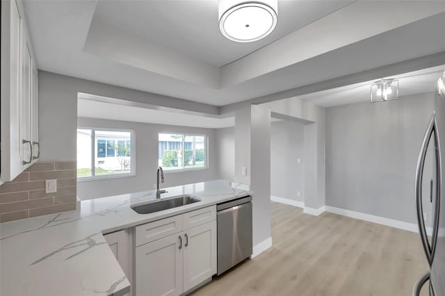 kitchen with decorative backsplash, appliances with stainless steel finishes, light stone counters, a tray ceiling, and a sink