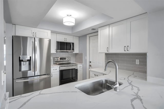 kitchen with light stone counters, stainless steel appliances, a sink, white cabinetry, and decorative backsplash