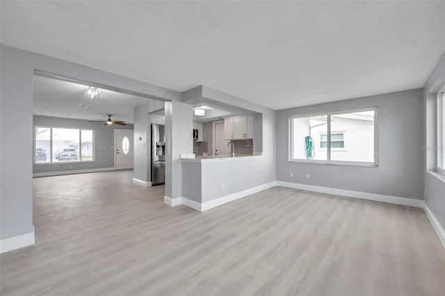 unfurnished living room with light wood finished floors, a textured ceiling, baseboards, and a ceiling fan