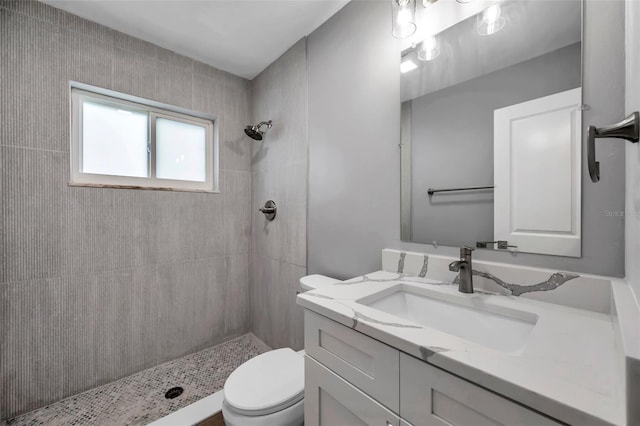 full bathroom with toilet, tiled shower, and vanity