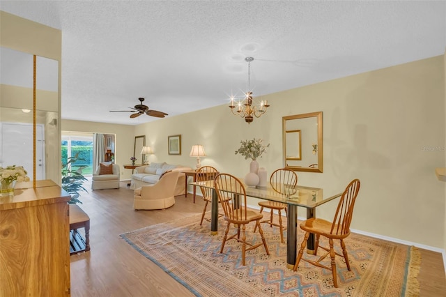 dining area with ceiling fan with notable chandelier, a textured ceiling, baseboards, and wood finished floors