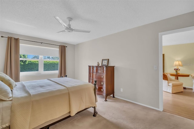 bedroom with light carpet, a textured ceiling, a ceiling fan, and baseboards