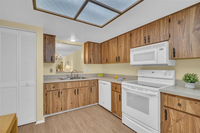 kitchen featuring light countertops, brown cabinetry, a sink, light wood-type flooring, and white appliances