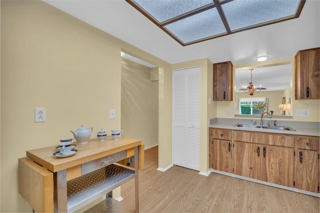 kitchen with light wood-type flooring, light countertops, a sink, and an inviting chandelier