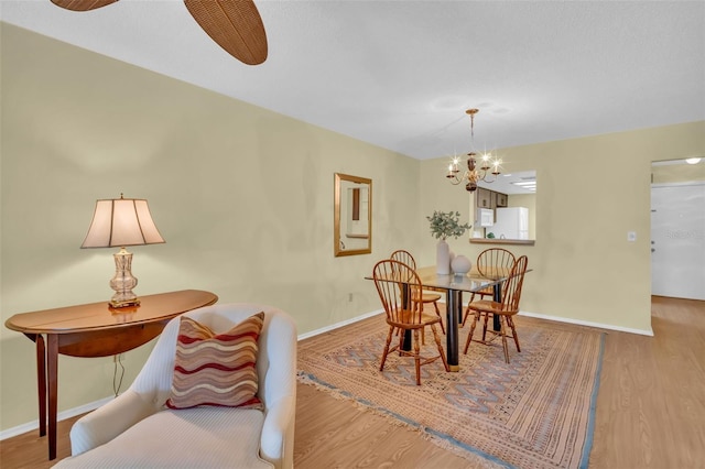 dining room with ceiling fan with notable chandelier, wood finished floors, and baseboards