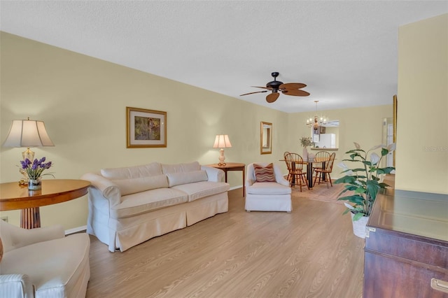 living room featuring baseboards, light wood-style flooring, a textured ceiling, and ceiling fan with notable chandelier