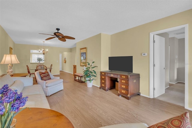 living area with a textured ceiling, ceiling fan with notable chandelier, light wood-style flooring, and baseboards