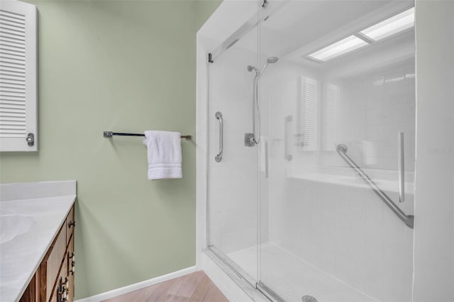 bathroom with wood finished floors, a shower stall, vanity, and baseboards