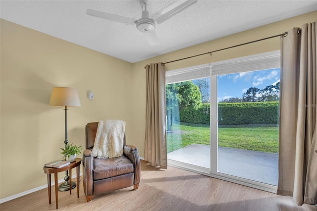 living area with a ceiling fan, a textured ceiling, baseboards, and wood finished floors