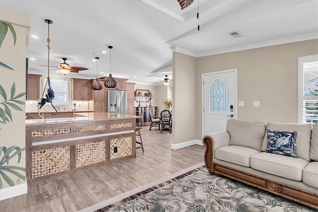 living area with visible vents, a ceiling fan, baseboards, ornamental molding, and light wood finished floors