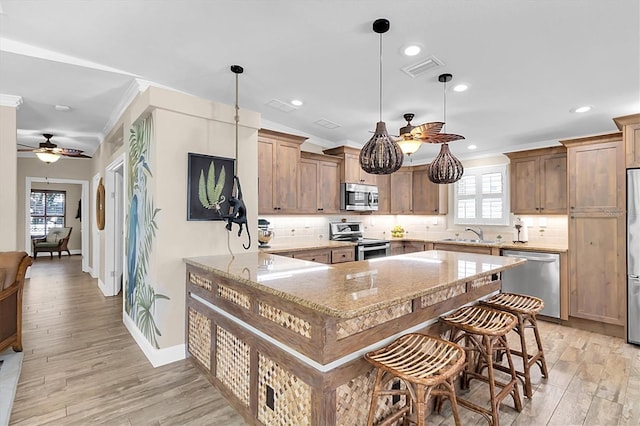 kitchen with light wood finished floors, appliances with stainless steel finishes, light stone counters, ornamental molding, and backsplash