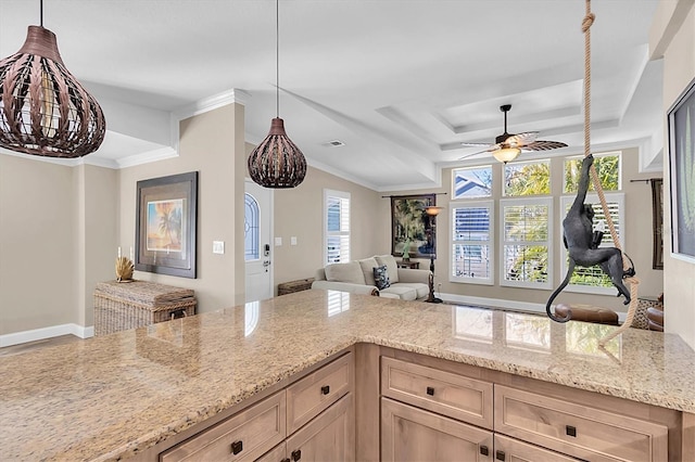 kitchen featuring a raised ceiling, hanging light fixtures, ornamental molding, open floor plan, and light stone countertops