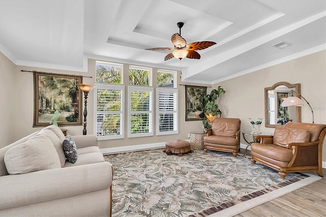 living area with baseboards, a ceiling fan, wood finished floors, a tray ceiling, and crown molding