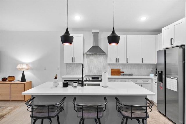 kitchen featuring wall chimney range hood, stainless steel fridge, white cabinets, and a kitchen breakfast bar