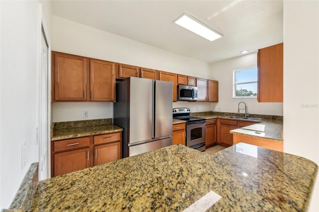 kitchen with stone countertops, appliances with stainless steel finishes, brown cabinets, and a sink