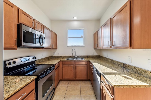 kitchen with brown cabinets, light tile patterned floors, stainless steel appliances, a sink, and light stone countertops