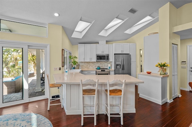 kitchen with vaulted ceiling with skylight, a peninsula, a sink, visible vents, and appliances with stainless steel finishes