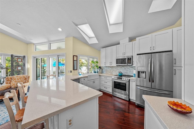 kitchen featuring light stone counters, tasteful backsplash, appliances with stainless steel finishes, lofted ceiling with skylight, and a peninsula