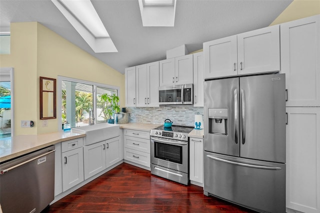 kitchen with appliances with stainless steel finishes, light countertops, a sink, and lofted ceiling with skylight