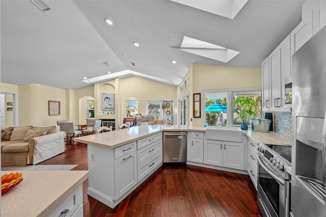 kitchen featuring a peninsula, vaulted ceiling with skylight, appliances with stainless steel finishes, and open floor plan