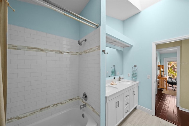 full bathroom with double vanity, shower / bath combination, a sink, wood finished floors, and baseboards