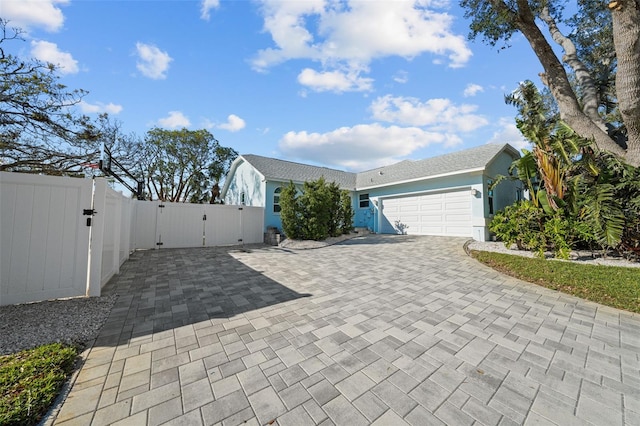 exterior space featuring decorative driveway, stucco siding, an attached garage, a gate, and fence