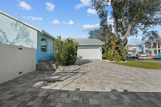 view of home's exterior with a garage, fence, decorative driveway, and stucco siding