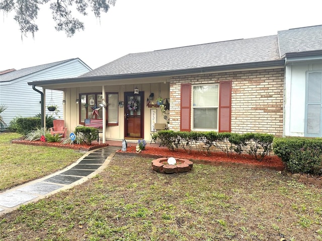 single story home featuring a shingled roof, a front yard, and brick siding