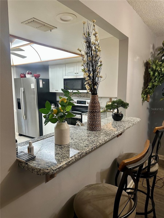 kitchen featuring visible vents, appliances with stainless steel finishes, a peninsula, a kitchen bar, and white cabinetry